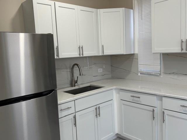 kitchen featuring backsplash, stainless steel fridge, sink, and white cabinetry