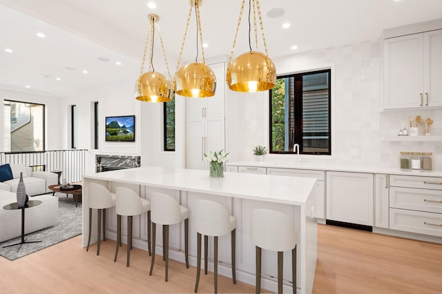 kitchen featuring hanging light fixtures, a breakfast bar, white cabinetry, and light hardwood / wood-style floors