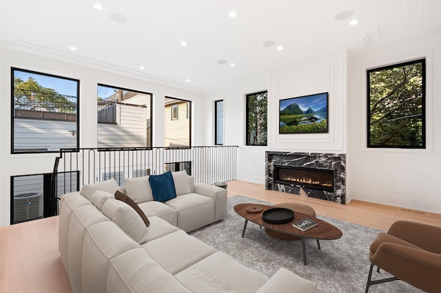 living room with a wealth of natural light, a premium fireplace, ornamental molding, and light hardwood / wood-style flooring