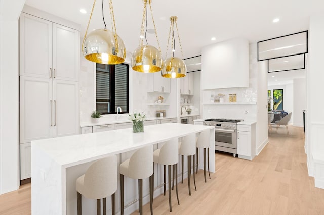 kitchen with light hardwood / wood-style floors, a kitchen island, pendant lighting, white cabinetry, and high end stainless steel range oven