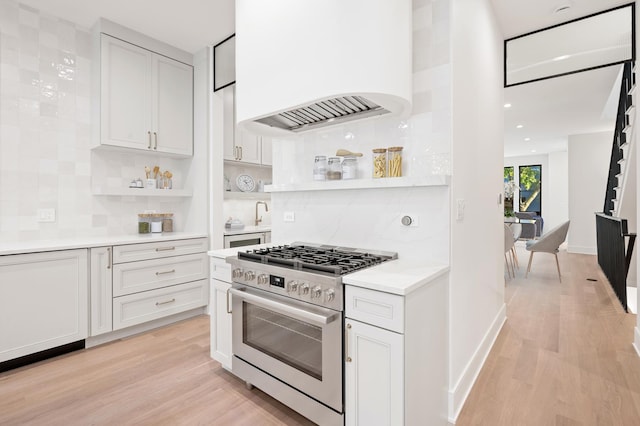 kitchen featuring custom exhaust hood, gas stove, tasteful backsplash, white cabinets, and light hardwood / wood-style flooring