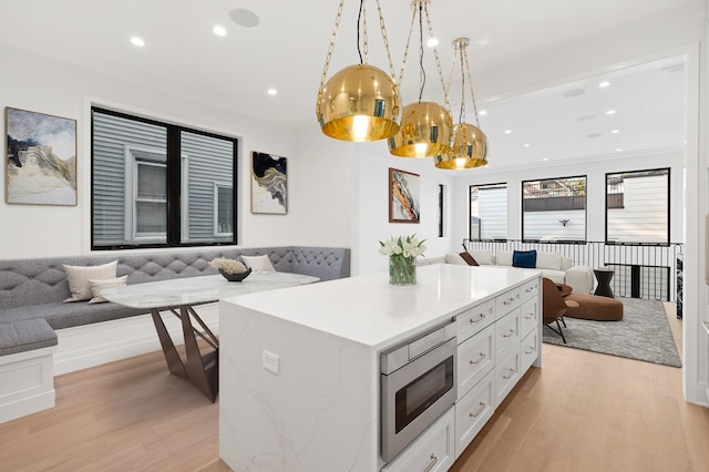 kitchen featuring a kitchen island, white cabinetry, hanging light fixtures, light wood-type flooring, and stainless steel microwave