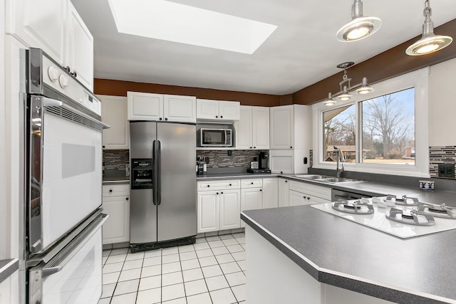 kitchen featuring sink, decorative light fixtures, a skylight, appliances with stainless steel finishes, and white cabinets