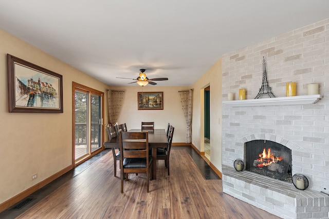 dining room with dark wood-type flooring, ceiling fan, and a brick fireplace