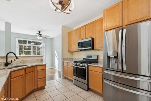 kitchen featuring sink, light tile patterned floors, ceiling fan, appliances with stainless steel finishes, and light stone counters