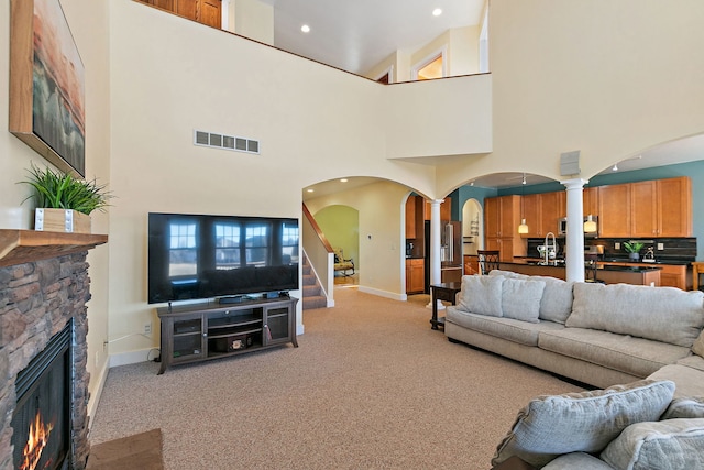 living room featuring light colored carpet, a fireplace, sink, and ornate columns