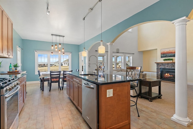 kitchen with decorative light fixtures, stainless steel appliances, decorative columns, and a center island with sink