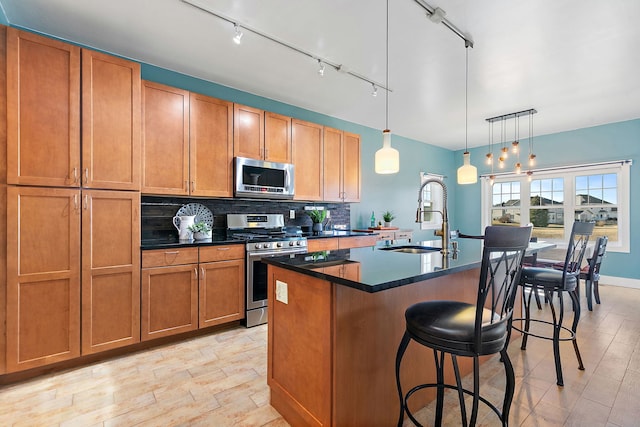 kitchen with sink, appliances with stainless steel finishes, backsplash, an island with sink, and decorative light fixtures