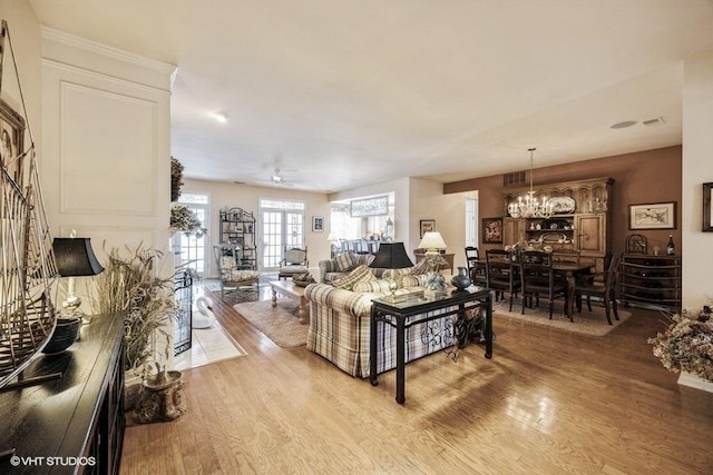 living room with ceiling fan with notable chandelier, a stone fireplace, and light hardwood / wood-style floors