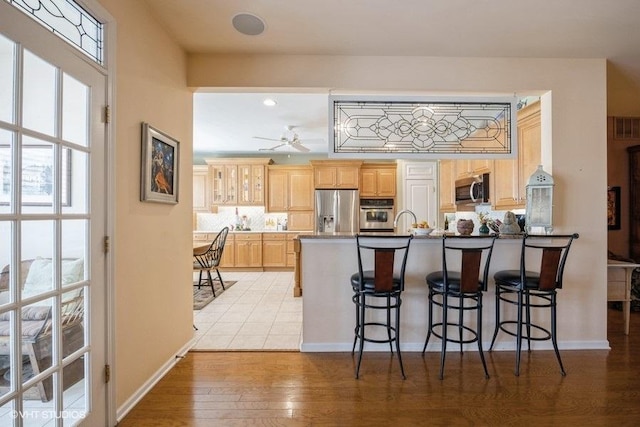 kitchen featuring a breakfast bar, ceiling fan, stainless steel appliances, light hardwood / wood-style floors, and light brown cabinets