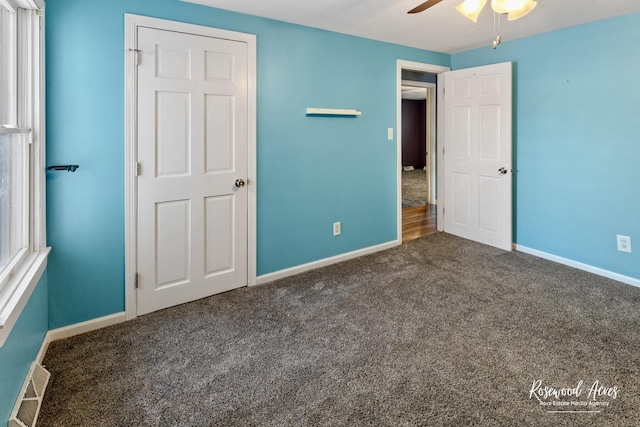 unfurnished bedroom with ceiling fan and dark colored carpet