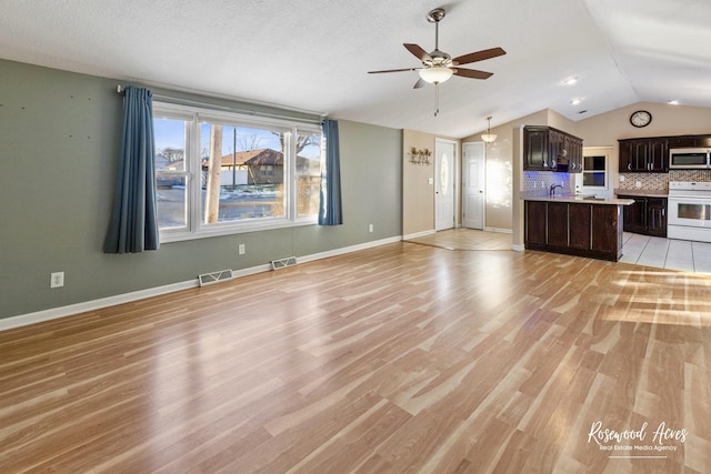 unfurnished living room with lofted ceiling, ceiling fan, sink, and light hardwood / wood-style floors