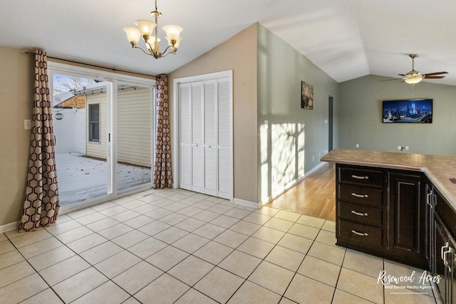 interior space with vaulted ceiling, pendant lighting, light tile patterned flooring, dark brown cabinets, and ceiling fan with notable chandelier