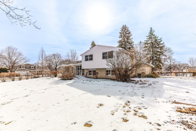 snow covered back of property featuring brick siding and a chimney