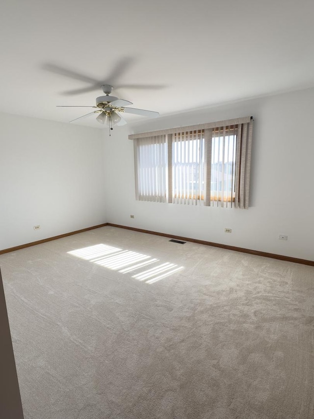 carpeted empty room featuring a ceiling fan, visible vents, and baseboards