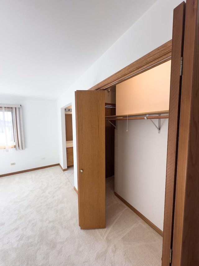 unfurnished bedroom featuring light carpet, baseboards, and a closet