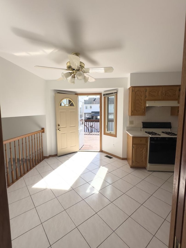 kitchen featuring light tile patterned floors, under cabinet range hood, light countertops, decorative backsplash, and range with gas cooktop