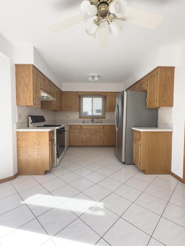 kitchen featuring light countertops, decorative backsplash, a sink, gas range, and under cabinet range hood