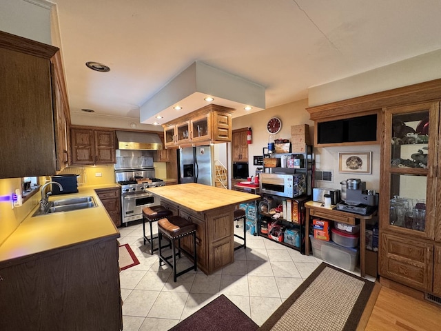 kitchen with a kitchen island, a breakfast bar, sink, light tile patterned flooring, and appliances with stainless steel finishes