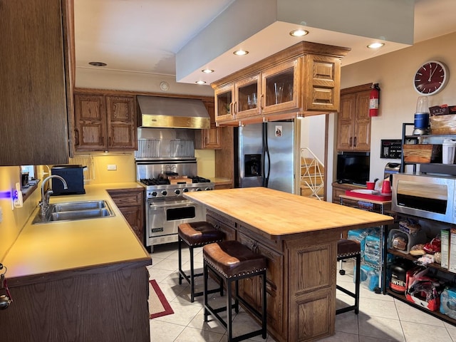 kitchen featuring light tile patterned floors, appliances with stainless steel finishes, a kitchen breakfast bar, wall chimney range hood, and sink