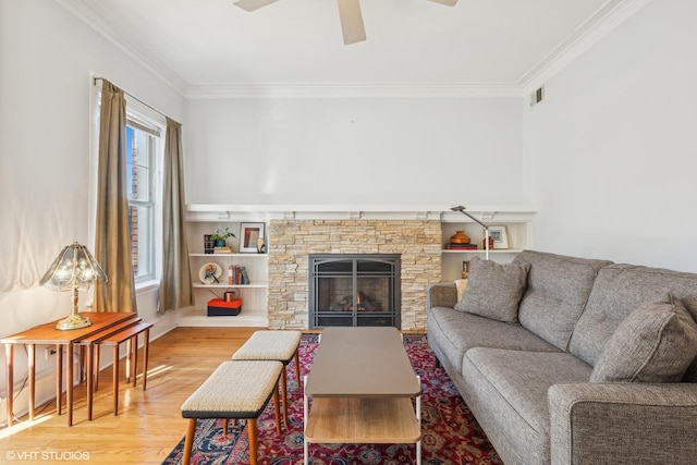 living room with crown molding, a stone fireplace, a wealth of natural light, and light wood-type flooring