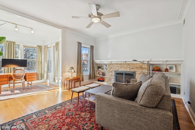 living room featuring ornamental molding, a stone fireplace, and wood-type flooring