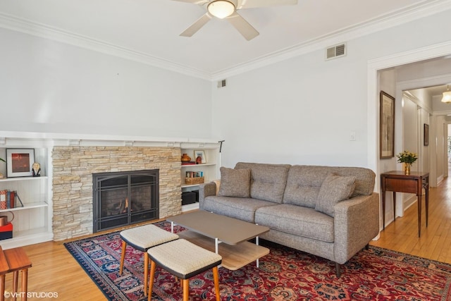 living room with ceiling fan, ornamental molding, a stone fireplace, and hardwood / wood-style floors