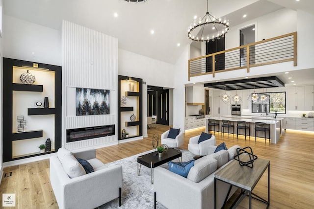 living room featuring light wood-type flooring, a towering ceiling, and a chandelier