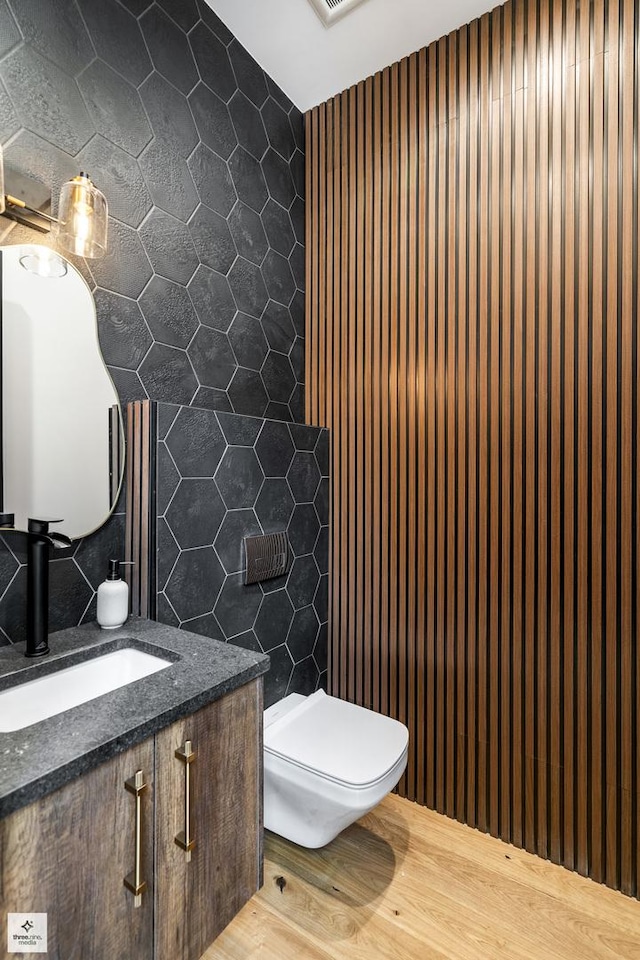 bathroom with wood-type flooring, vanity, tasteful backsplash, tile walls, and toilet