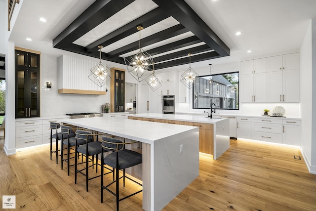 kitchen with white cabinetry, a spacious island, light wood-type flooring, pendant lighting, and a breakfast bar