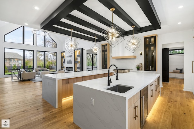 kitchen with light wood-type flooring, decorative light fixtures, a large island with sink, and sink