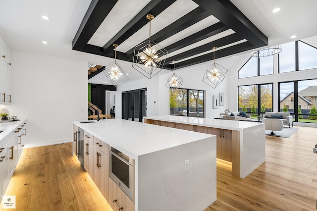 kitchen featuring a spacious island, hanging light fixtures, a notable chandelier, stainless steel microwave, and light hardwood / wood-style flooring