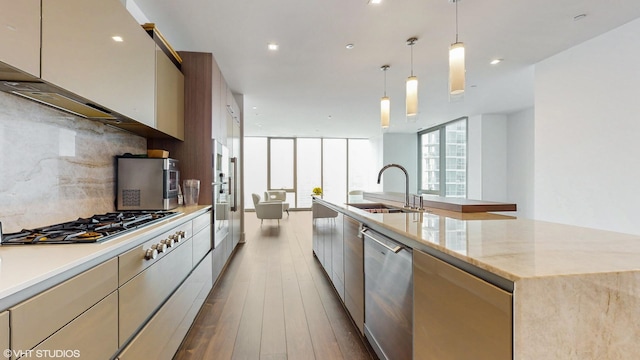 kitchen with appliances with stainless steel finishes, decorative backsplash, a spacious island, light stone counters, and sink