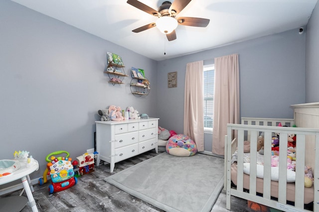 bedroom featuring dark wood-type flooring, ceiling fan, and a crib