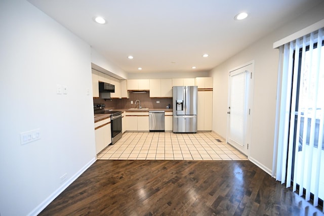 kitchen featuring white cabinetry, stainless steel appliances, tasteful backsplash, light wood-type flooring, and sink