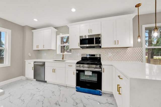 kitchen with a wealth of natural light, appliances with stainless steel finishes, white cabinets, and hanging light fixtures