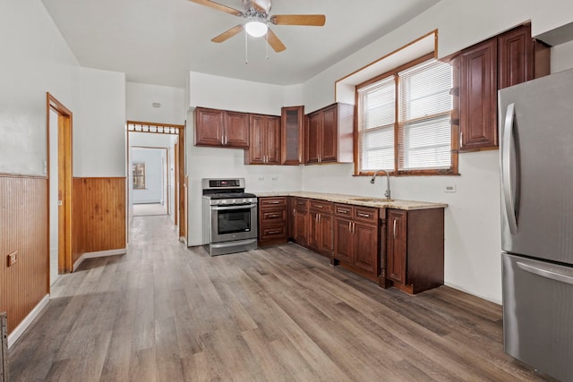 kitchen with wooden walls, ceiling fan, stainless steel appliances, light hardwood / wood-style flooring, and sink