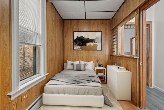 bedroom featuring multiple windows, a baseboard heating unit, and wooden walls