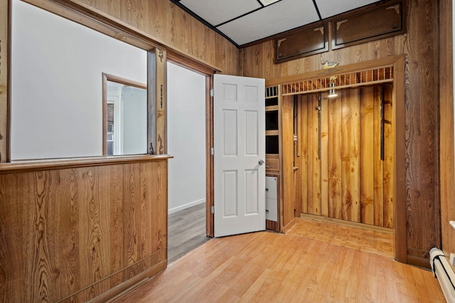 hallway with a baseboard radiator, light wood-type flooring, and wooden walls