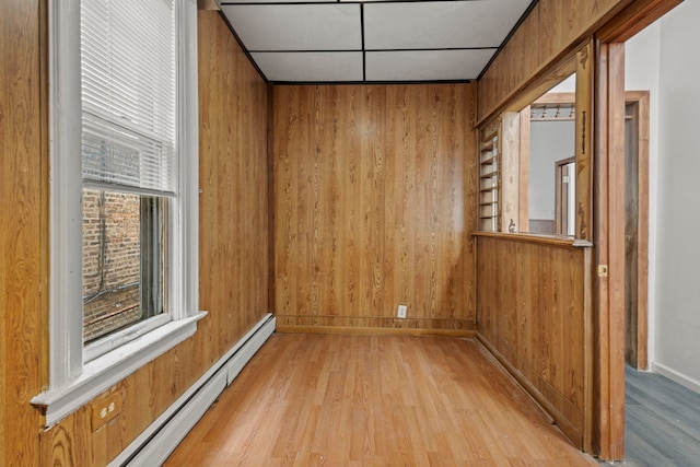 unfurnished room featuring a baseboard heating unit, wooden walls, and light hardwood / wood-style floors