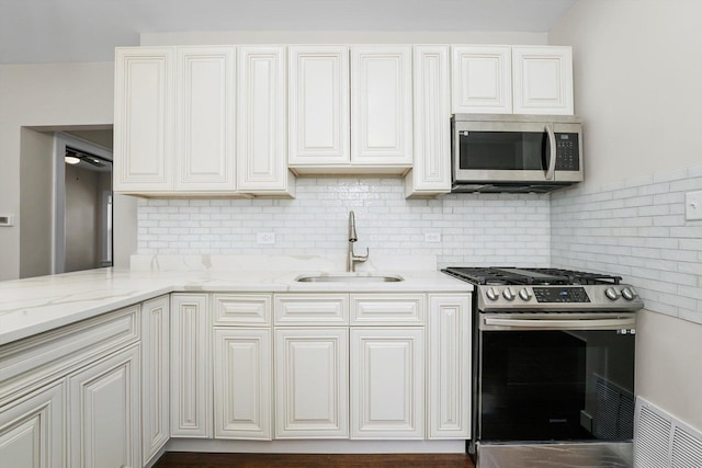 kitchen featuring decorative backsplash, sink, white cabinetry, appliances with stainless steel finishes, and light stone counters