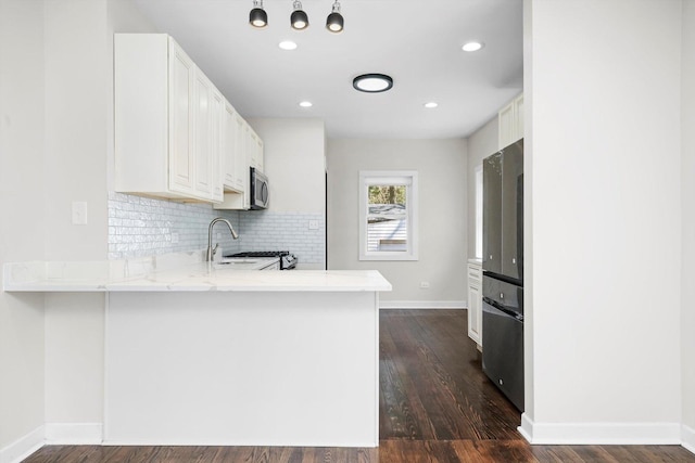 kitchen featuring kitchen peninsula, appliances with stainless steel finishes, dark hardwood / wood-style floors, white cabinets, and sink