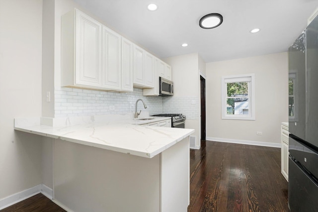 kitchen with white cabinetry, kitchen peninsula, appliances with stainless steel finishes, light stone countertops, and sink