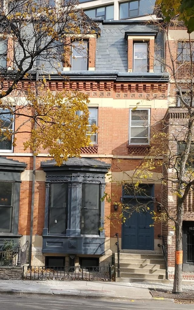 view of front of property featuring entry steps, brick siding, and mansard roof