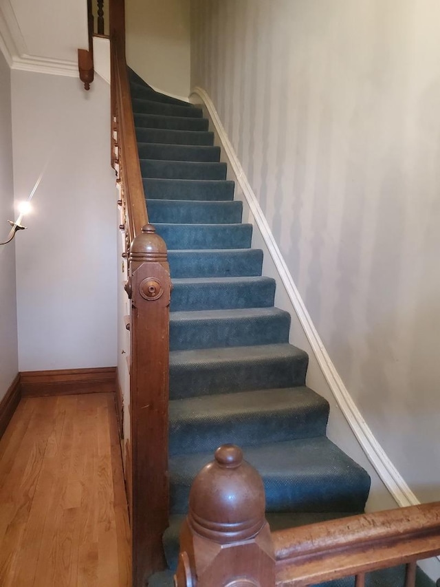 stairway with crown molding, wood finished floors, and baseboards