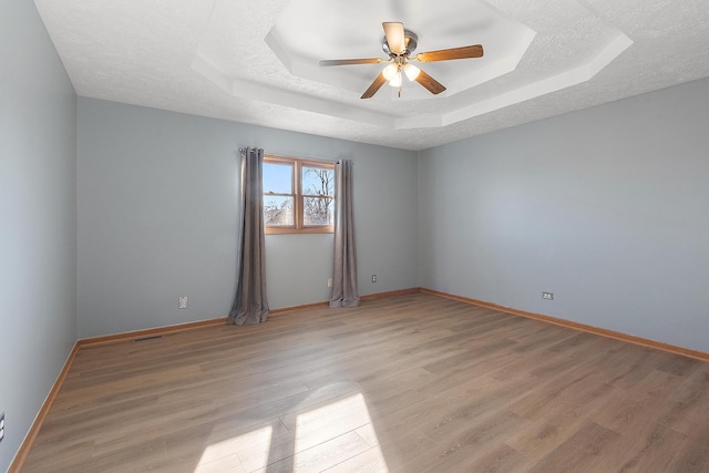 unfurnished room with a raised ceiling, ceiling fan, and light hardwood / wood-style flooring