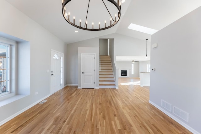 unfurnished living room featuring light hardwood / wood-style floors, plenty of natural light, high vaulted ceiling, and a chandelier