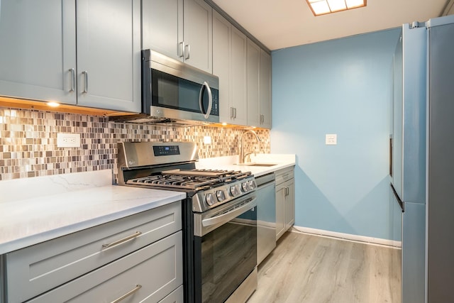 kitchen featuring stainless steel appliances, tasteful backsplash, light hardwood / wood-style floors, sink, and gray cabinets