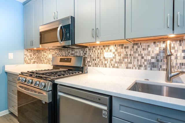 kitchen featuring wood-type flooring, sink, light stone counters, decorative backsplash, and stainless steel appliances