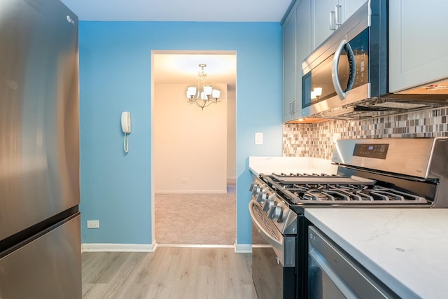 kitchen with appliances with stainless steel finishes, decorative light fixtures, light hardwood / wood-style flooring, an inviting chandelier, and backsplash